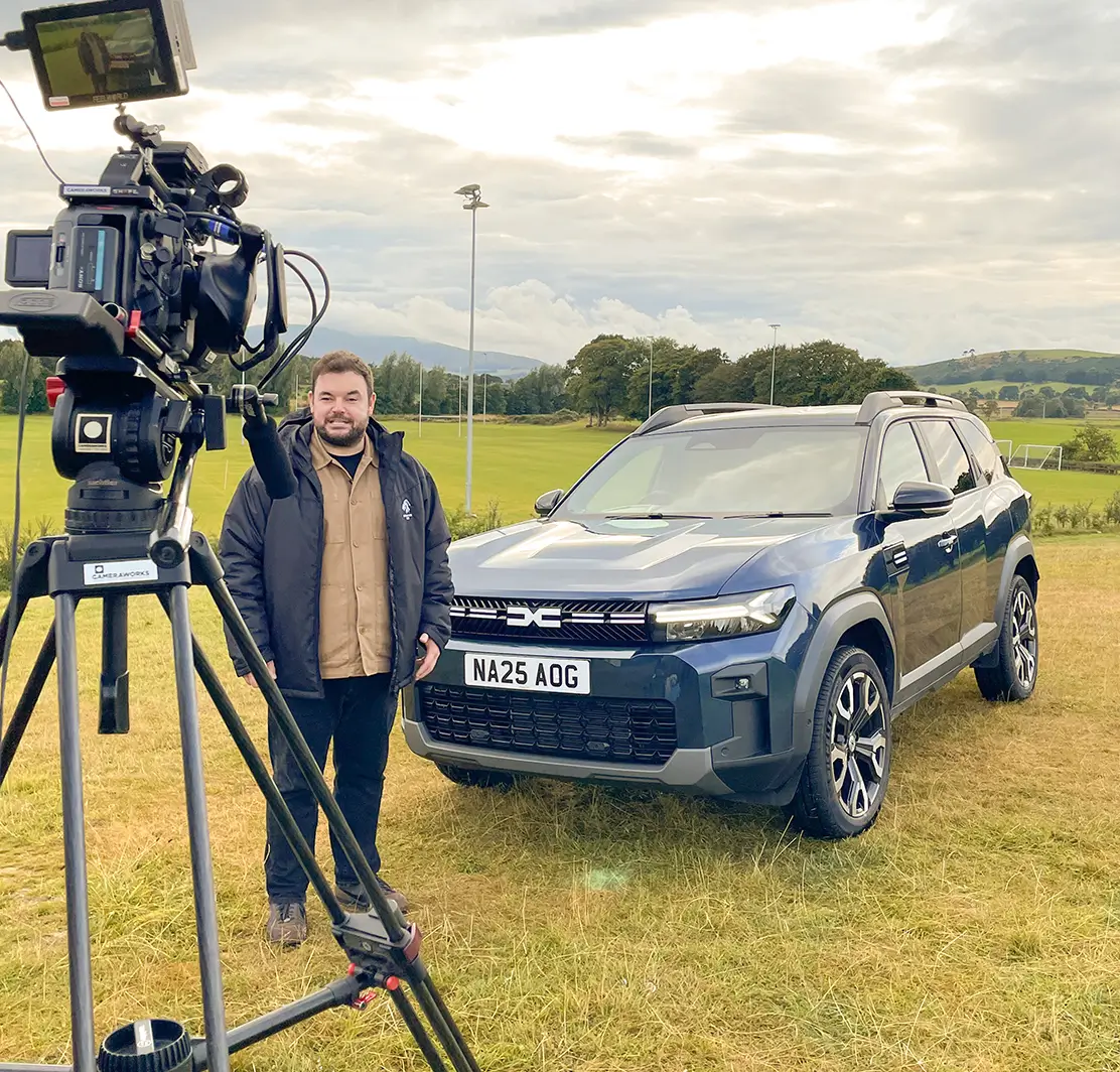 A young man dribbles a basketball on an outdoor court, looking towards the camera.